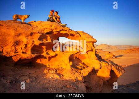 Turista con un cane che guarda sulle sabbie rosse del deserto di Wadi Rum nel tempo del tramonto, Giordania Foto Stock