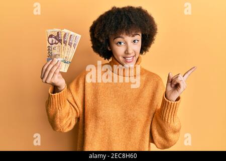 Giovane ragazza ispanica che tiene 5000 banconote forint ungheresi sorridenti felici puntare con la mano e il dito verso il lato Foto Stock