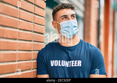 Giovane volontario ispanico che indossa una maschera medica in piedi in città. Foto Stock