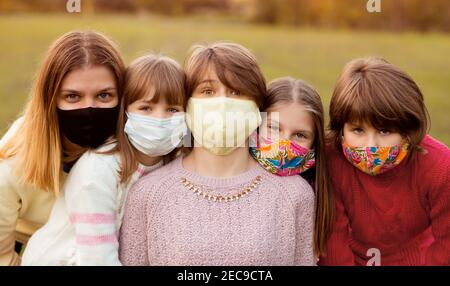Gruppo di bambini in maschere mediche protettive camminano per strada al tramonto d'autunno. Quarantena concettuale Foto Stock
