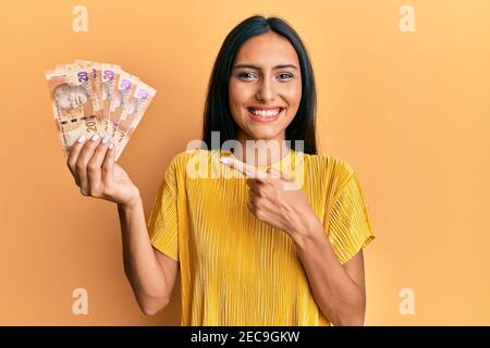 Giovane donna bruna che tiene in mano banconote da 20 rand sudafricane sorridenti buon puntamento con mano e dito Foto Stock