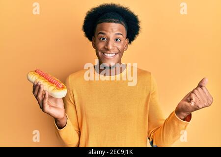 L'uomo afroamericano con i capelli afro mangiare hotdog gridando orgoglioso, celebrando la vittoria e il successo molto eccitato con il braccio sollevato Foto Stock