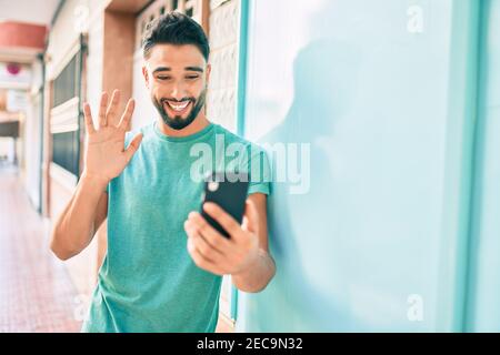 Giovane arabo sorridente felice di videochiamare con lo smartphone in città. Foto Stock