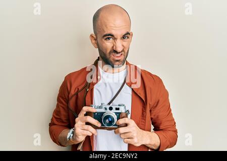 Giovane uomo ispanico che tiene la macchina fotografica vintage indistato e confuso espressione. Dubbio concetto. Foto Stock