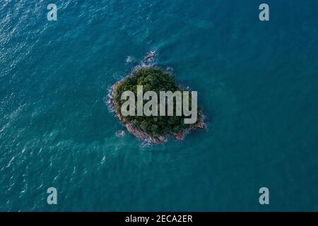 Vista aerea di una piccola isola rocciosa coperta di verde nel mezzo dell'oceano di colore turchese Foto Stock