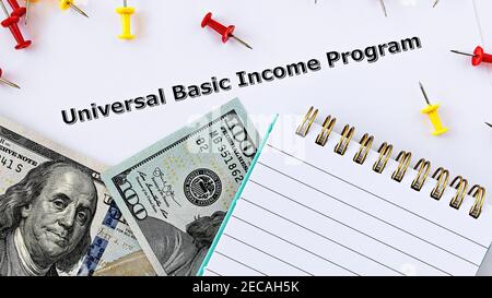 Foto in primo piano sul tema reddito base universale. Le parole Universal Basic Income Program sulla carta, circondato da banconote e blocco note Foto Stock