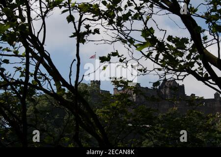 Castello di Edimburgo, Edimburgo, Scozia. Incorniciato da alberi e visto da Princess Street Gardens. Con la bandiera dell'Unione. Foto Stock