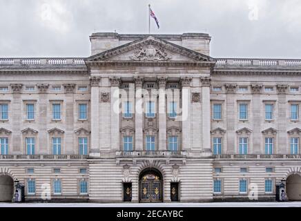 La facciata di Buckingham Palace con Queens Footguard soldati in servizio, neve d'inverno, nuvole scure, Londra, Regno Unito Foto Stock