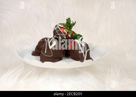 fragole ricoperte di cioccolato su piastra a piedistallo bianca e pelliccia Foto Stock