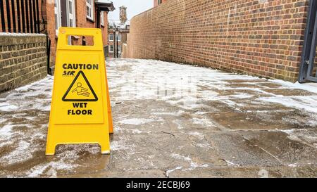 Un cartello di attenzione sul pavimento bagnato che segnala il pericolo di  scivolamento su un percorso ghiacciato Foto stock - Alamy