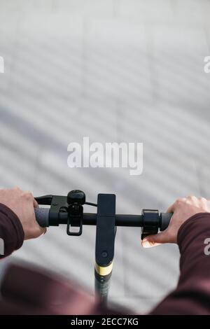 Primo piano delle mani di una persona che tiene il manubrio di uno scooter elettrico. Fotografia verticale. Foto Stock