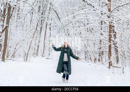 Donna in giacca verde blu parka abiti invernali e cappello a piedi vagando nel parco foresta all'aperto nella neve giorno invernale. Buon viaggiatore da solo esplorando lo Foto Stock