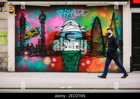 Londra, Regno Unito. 12 Feb 2021.UN uomo con una maschera facciale cammina attraverso Paramedic e Covid-19 Street art su Oxford Street. Credito: Waldemar Sikora Foto Stock