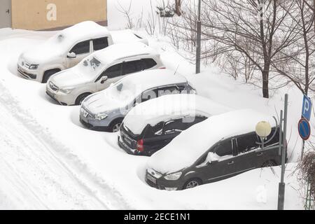 Mosca / Russia - Febbraio 13 2021: Auto in strada parcheggio vicino appartamento edificio sotto uno spesso strato di neve, nel pomeriggio, dopo notte tempesta di neve. Str Foto Stock