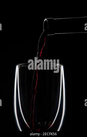 Vino rosso versato in un bicchiere di vino su un sfondo nero Foto Stock