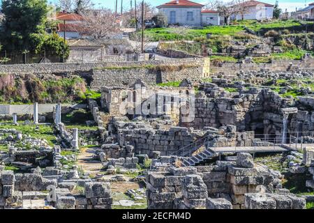 Scavi archeologici rovine in antica Corinto Grecia con scale e. passerella per i turisti e case di villaggio con tetto in tegole rosse dietro Foto Stock