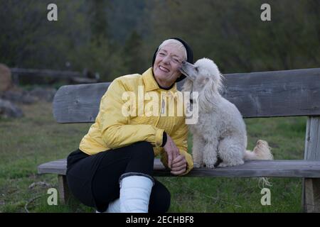 Una donna anziana e il suo poodle godono la vita all'aperto in una fredda giornata di primavera. Foto Stock