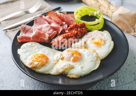 primo piano vista sul lato soleggiato fino uova prosciutto coppa Capocollo di carne secca e insalata di paprika ajvar fatta in casa in piatto sul tavolo come cena o colazione Foto Stock