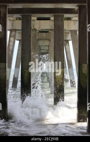 Onde che si schiantano su pali di cemento sotto il molo Foto Stock