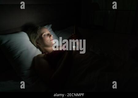 donna a letto prima di andare a dormire con il telefono in mano Foto Stock