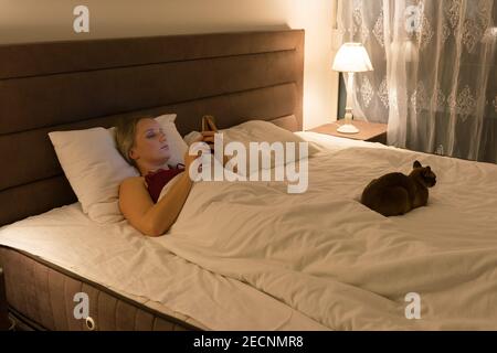 donna a letto prima di andare a dormire con il telefono in mano Foto Stock