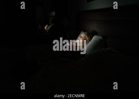 donna a letto prima di andare a dormire con il telefono in mano Foto Stock