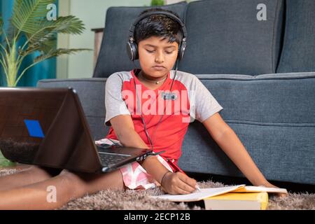 bambino con cuffie che annotano fino a prenotare dal laptop durante la lezione virtuale dal laptop a casa - concetto di classe online, formazione online Foto Stock