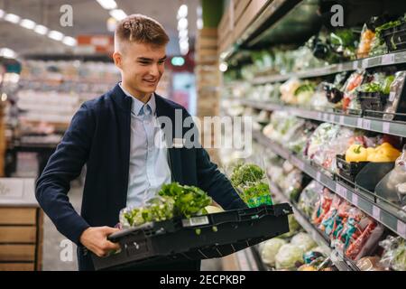 Assistente di negozio nel supermercato riapprovvigionamento verdure fresche in scaffali della sezione prodotti. Foto Stock