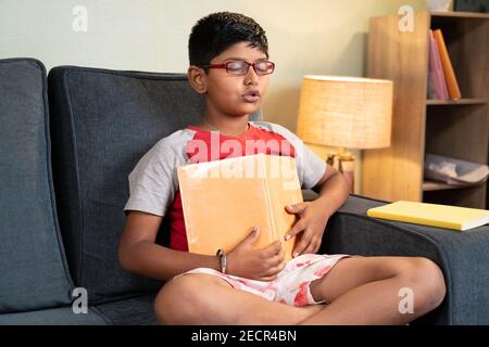 ragazzino che agguda le risposte dal libro durante gli esami con fuori capire i concetti a casa sul divano - concetto del sistema di istruzione e adolescente Foto Stock