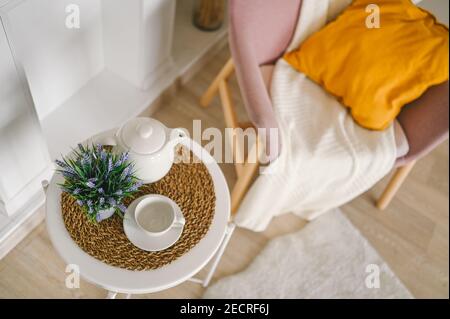 Elegante ed elegante eco composizione soggiorno con tavolo da colazione bianco tazza caffè teapot falso camino fiori secchi piante pampas erba rosa poltroncina polvere, coperta e cuscino. Arredamento moderno. Foto Stock