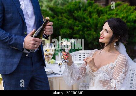 Ritratto di una giovane coppia felice newlywed che festeggia il matrimonio con bottiglia di champagne al parco Foto Stock