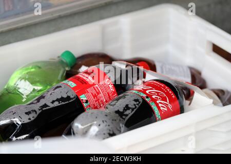Bottiglie di soda Coca-Cola in plastica e altre bottiglie di limonata in un grande contenitore bianco. Bevande malsane ma deliziose. Primo piano. Foto Stock