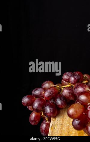Vista dall'alto di mazzo di uve rosse umide, su tavola rustica in legno e fondo nero, in verticale Foto Stock