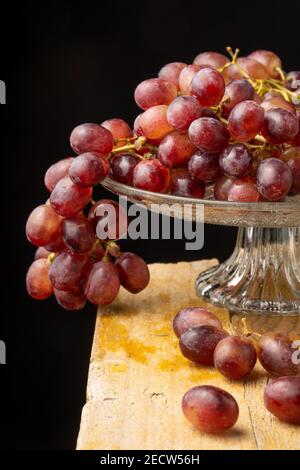 Vista dei grappoli d'uva rossa in stativo di vetro, su tavolo di legno, con fuoco selettivo, fondo nero, verticale Foto Stock