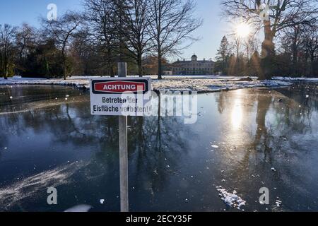 Cartello segnaletico con l'iscrizione "attenzione, tenere lontano dalla superficie ghiacciata" presso il laghetto congelato del giardino del palazzo preferito di Schloss a Förch, Germania Foto Stock