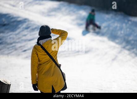 Berlino, Germania. 14 Feb 2021. Una madre guarda il suo bambino che slitta giù per una collina nel parco di Görlitzer. Credit: Fabian Sommer/dpa/Alamy Live News Foto Stock