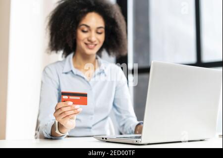 Donna d'affari multirazziale di successo con capelli ricci, sorridente, seduto al portatile, pagando dentro Internet,acquisto online,lavoro dall'ufficio Foto Stock