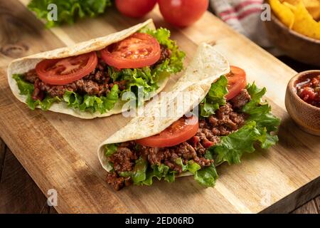 Tacos di manzo con lattuga e pomodoro su un taglio di legno tavola con tortilla chips e salsa in background Foto Stock