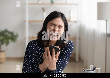 Ridendo millennial asian donna che guarda carino commedia online per telefono Foto Stock