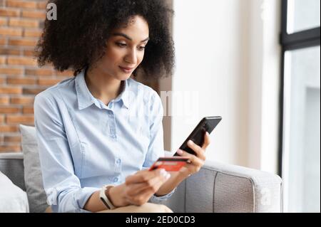 Primo piano di una donna d'affari afro-americana mista-corsa con capelli ricci che tengono il telefono cellulare, inserendo il numero della carta di credito per fare un online Foto Stock