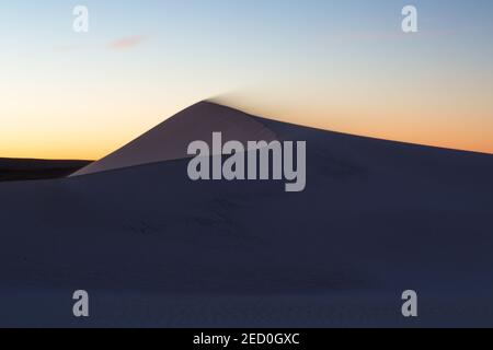 Colori dorati dell'alba dietro le dune di sabbia con vento che soffia la sabbia fuori dalle dune, Jurien Bay, Australia Occidentale Foto Stock