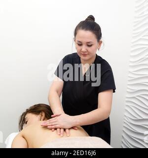 Salone di bellezza con centro massaggi classico, massaggiatrice giovane in tuta nera. Foto Stock