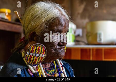 Chin Kaang Hill-tribù donna con tatuaggio facciale tradizionale e elaborati orecchini tribali che giocano un flauto con il naso, Mindat, Chin stato, Myanmar Foto Stock