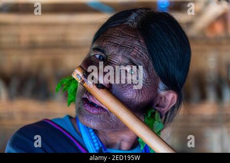 Donna di mento con tatuaggio spiderweb che soffia un flauto con il naso, Kanpelet, Chin stato, Myanmar Foto Stock