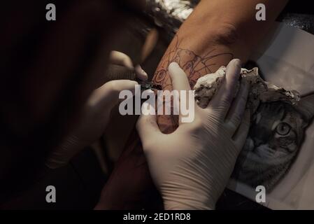 Dall'alto di tatuista maschile irriconoscibile utilizzando la macchina e la fabbricazione tatuaggio sul braccio del cliente di raccolto in salone Foto Stock