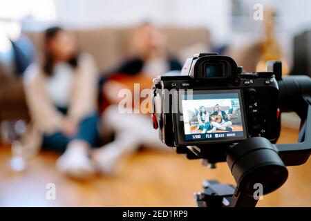 Coppia creativa di musicisti seduti a terra e riprese video sulla fotocamera mentre si suona la chitarra acustica per i social media blog Foto Stock