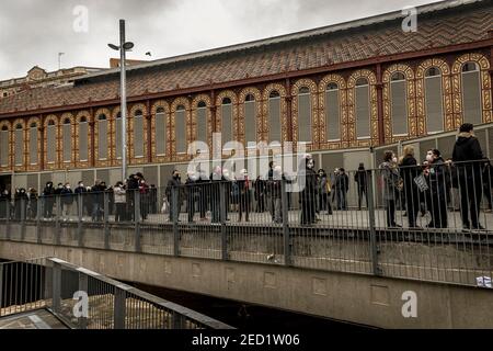 Barcellona, Spagna. 14 Feb 2021. Gli elettori che indossano maschere facciali protettive si accodano mantenendo la distanza sociale di fronte a una stazione elettorale per lanciare il loro voto in una casella elettorale per le 13 elezioni regionali della Catalogna sotto rigorosi protocolli sanitari in una terza ondata del COVID-19 pandemic Credit: Matthias Oesterle/Alamy Live News Foto Stock