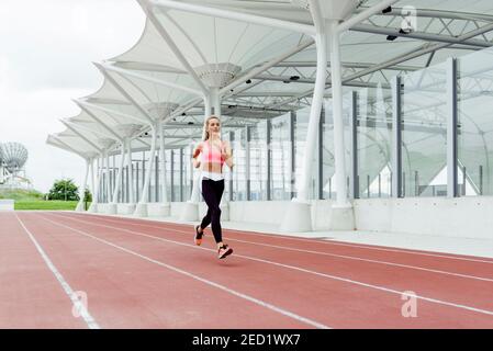 Attraente giovane sportivo in abbigliamento sportivo che corre su pista Foto Stock