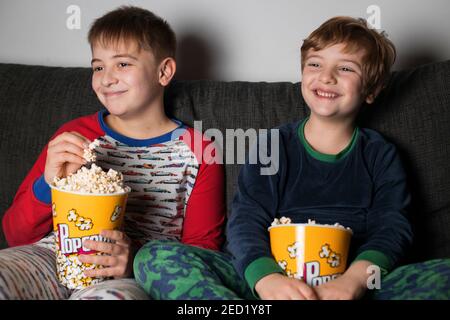 I piccoli fratelli giovani si siedono comodi sul divano con secchio di popcorn Mentre si mangia e si guarda la TV Foto Stock