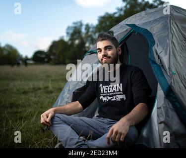 Un attivista maschile di Animal Rebellion siede all'ingresso della sua tenda in un campeggio a Brockwell Park, Londra, 31 agosto 2020 Foto Stock